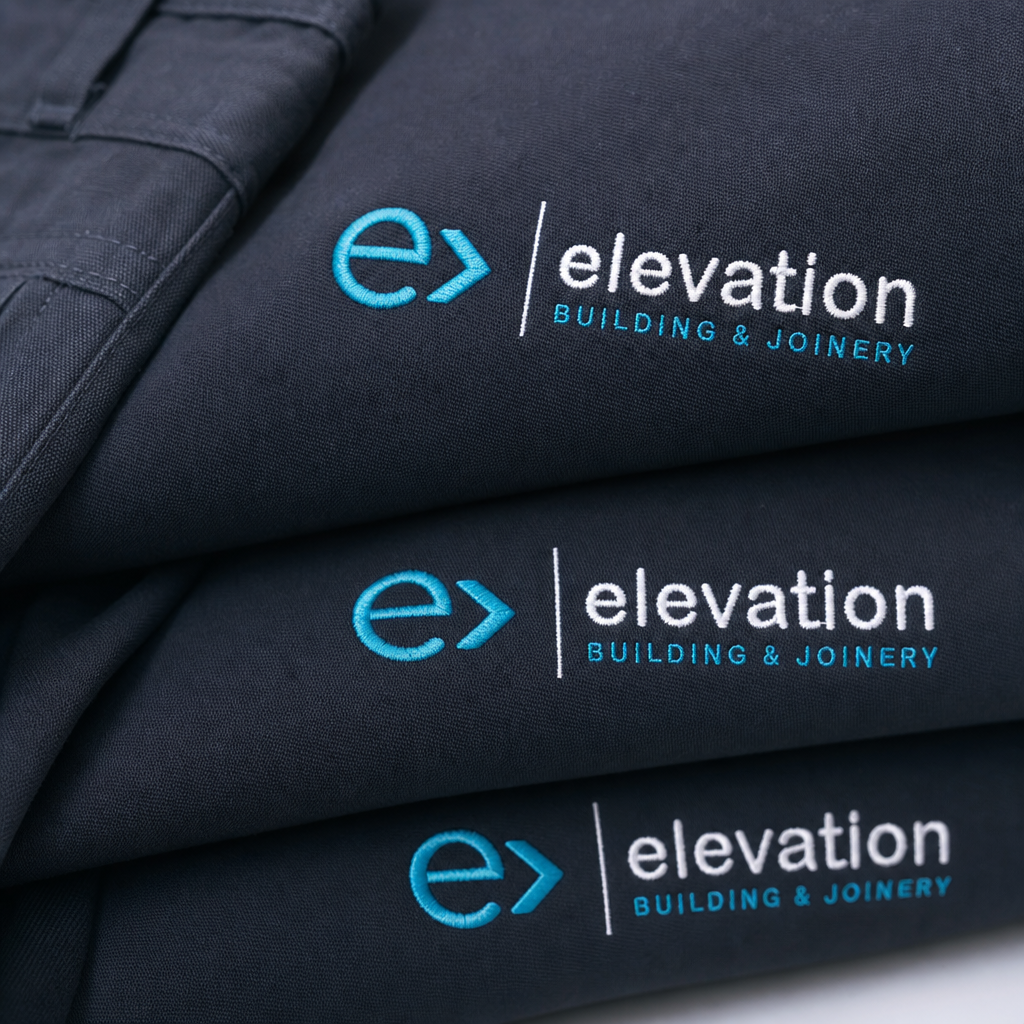 Close-up of embroidered branding details on workwear showing consistent quality across stacked garments