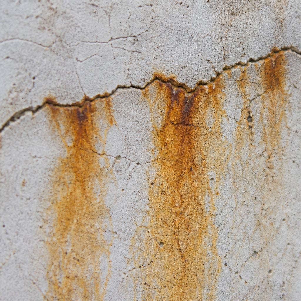 Fissures linéaires et taches ocre sur béton armé dégradé
