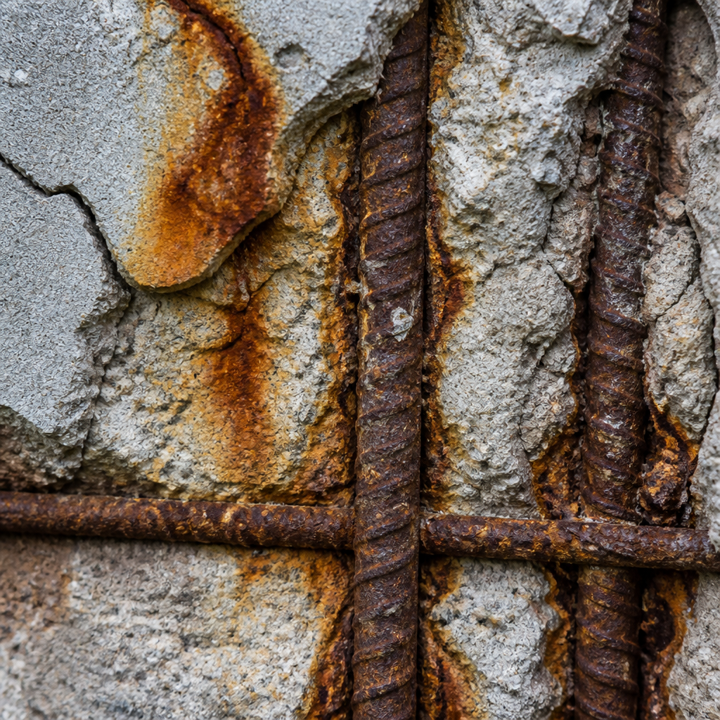 Rouille visible sur les armatures d'acier dégradant le béton avec taches d'oxydation orange et effondrement de surface