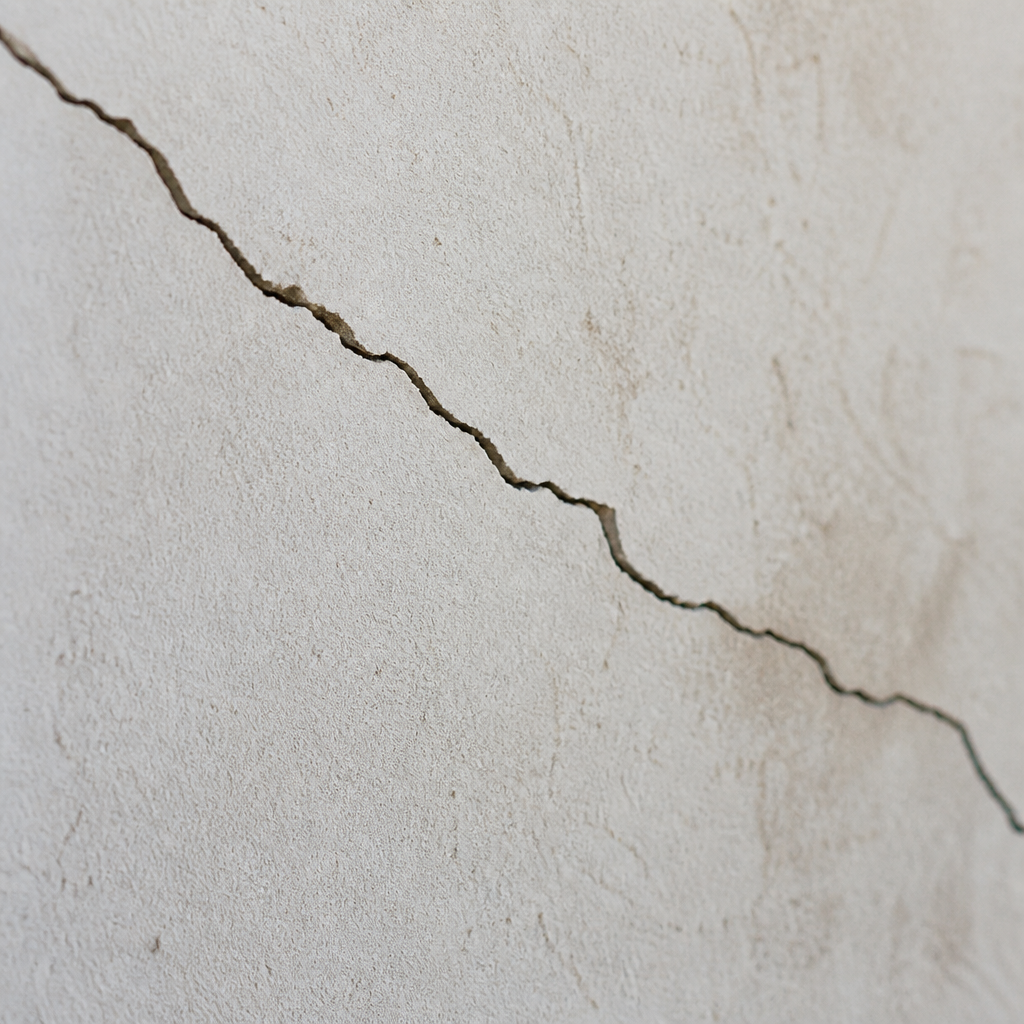 Gros plan d'une fissure structurelle fine sur une surface murale en plâtre.